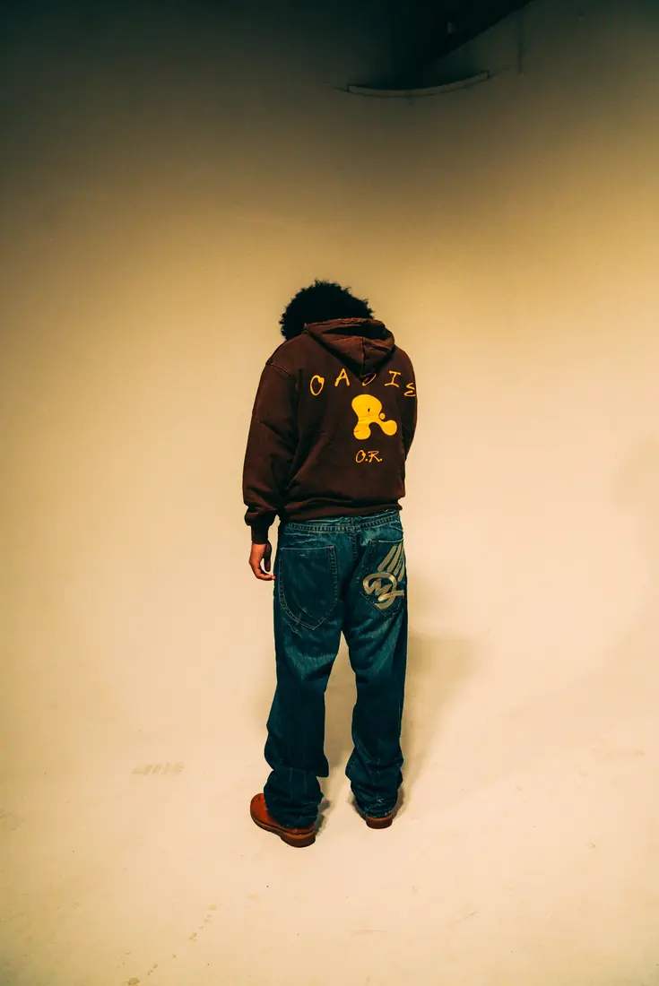 OASIS hoodie back view in an empty studio room